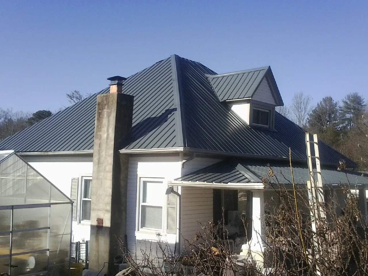 Dark blue standing seam metal roof on a white farmhouse with dormer — Slate & Tile Roof Repair by Roofing Brothers in Chesapeake Beach