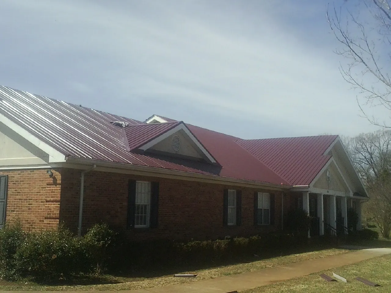 Red metal roof with gabled entries on a long brick building, from a Hail Damage Roof Repair job in Chesapeake Beach