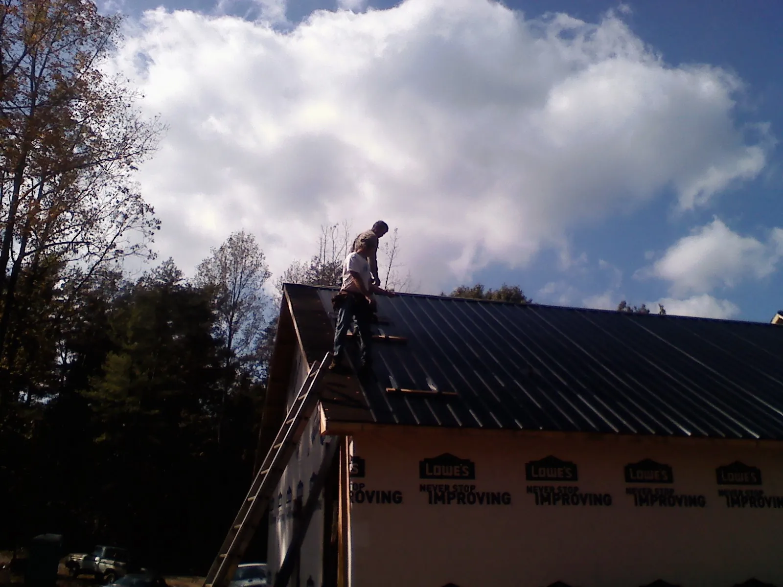 Roofer fastening dark metal panels high against a cloudy sky, from a Roof Inspection job in Chesapeake Beach