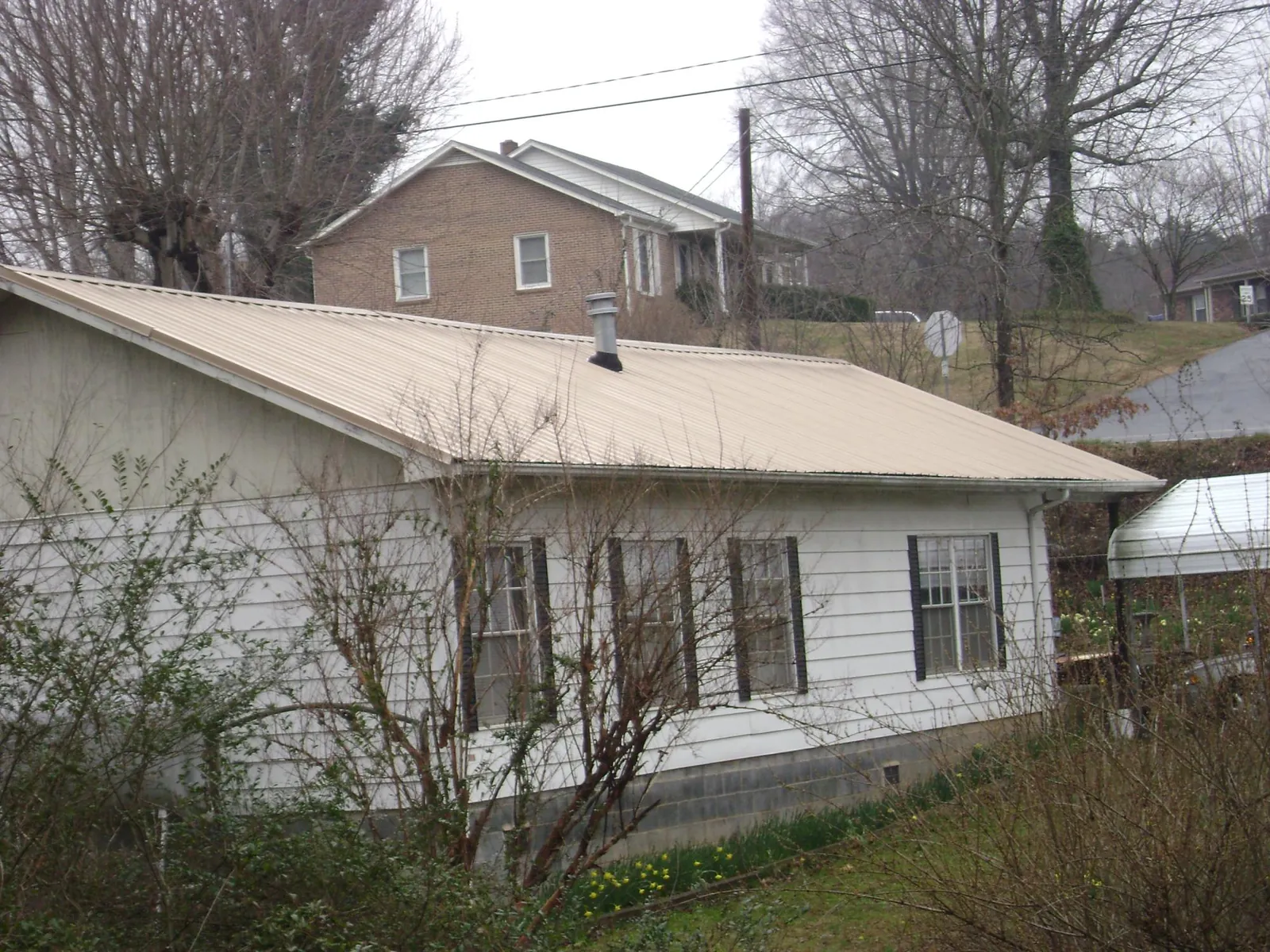 Tan metal roof on a white sided house set into a hillside — Commercial Roofing by Roofing Brothers in Chesapeake Beach